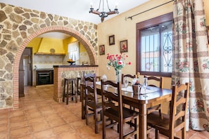 Un comedor con un arco de piedra, sillas de madera, una mesa con un jarrón de flores y vistas a la cocina.