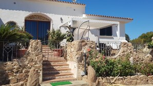A white building with a blue door, stone steps, and a garden with plants and a lamp post. - Beautiful Sun House Villa with Sea View, Wi-Fi, Balcony & Terrace (Cannigione)