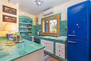 A kitchen with a blue refrigerator, white cabinets, a window with a decorative frame, and a tiled backsplash. - Beautiful Sun House Villa with Sea View, Wi-Fi, Balcony & Terrace (Cannigione)