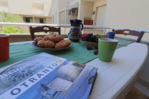 Une table avec une assiette de pâtisseries, une carafe, un bol de raisins et un magazine, le tout posé sur un balcon.