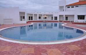 Une piscine à bord incurvé, entourée d’une terrasse carrelée et de murs blancs.