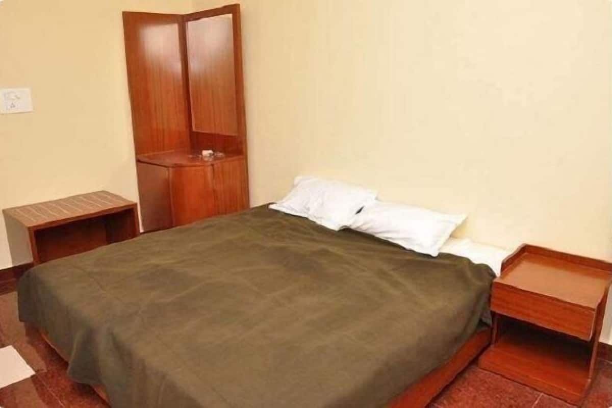 Een enkel bed met een groene sprei, houten nachtkastjes en een houten garderobe in een kamer met eenvoudige muren.