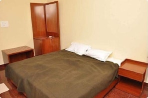 A single bed with a green bedspread, wooden nightstands, and a wooden wardrobe in a room with plain walls. - Ulo Millionaire Park (Chennai)