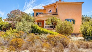 A two-story building with a balcony, surrounded by various shrubs and trees. - Beautiful and Spacious Villa in a Quiet Location with Large Pool, Terrace, Balcony & Garden (Campos)