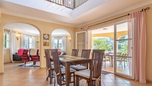 A spacious dining area with a high ceiling, large windows, and a view of the outdoors. - Beautiful and Spacious Villa in a Quiet Location with Large Pool, Terrace, Balcony & Garden (Campos)