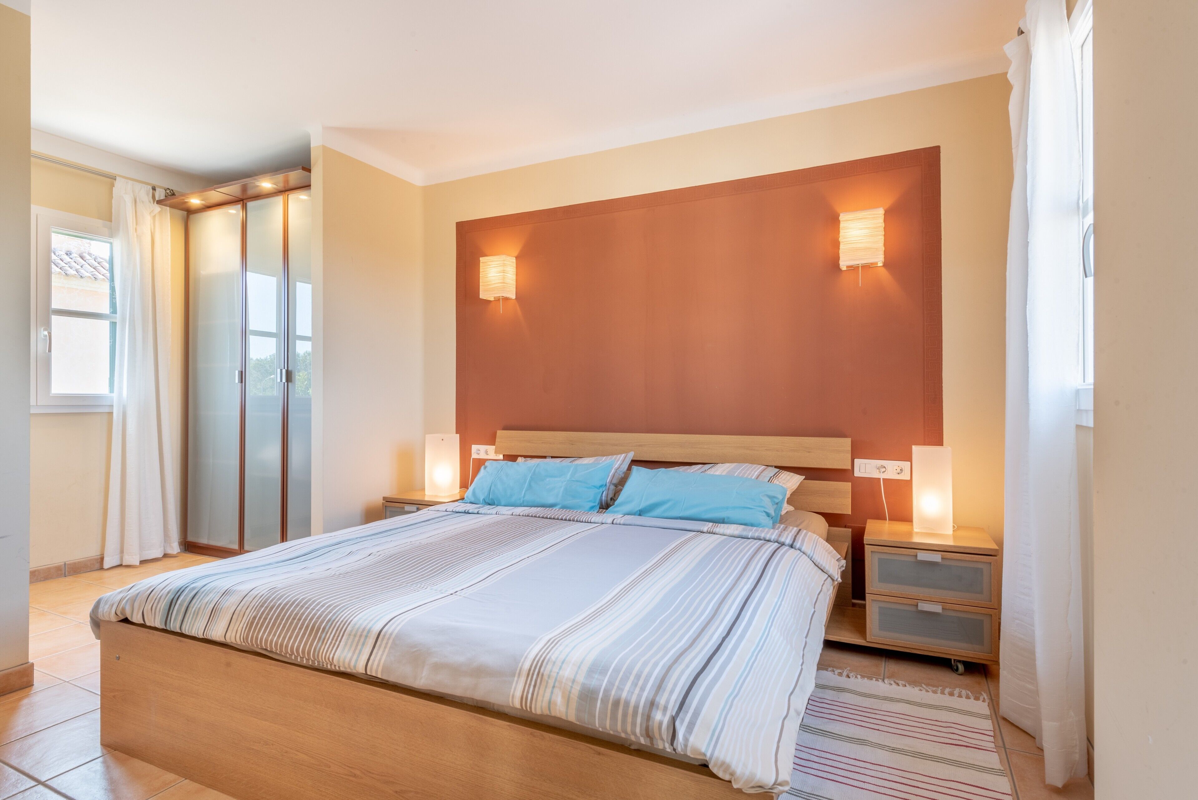 Un dormitorio con una cama grande, dos mesitas de noche, un cabecero de madera y dos lámparas de pared.