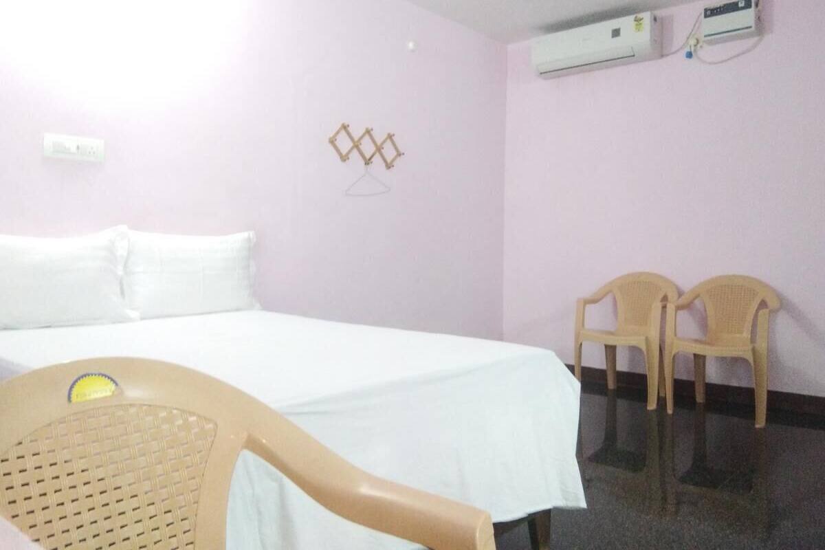 Habitación de hotel con una cama, dos sillas de plástico y un equipo de aire acondicionado en la pared.