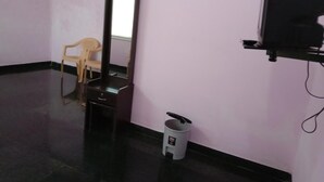 Ein Zimmer mit Spiegel, Stuhl, Mülleimer und Fernseher auf einem Standfuß.