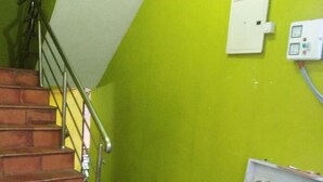 Eine Treppe mit Metallgeländer, einer grünen Wand, einer weißen Stromdosenleiste und einem Regal mit Büchern und Papieren.