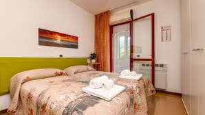 A bedroom with two beds, a painting of a sunset, a red-framed mirror, and a green accent wall. - Charming Lake Garda Home - Civic 55 (Toscolano Maderno)