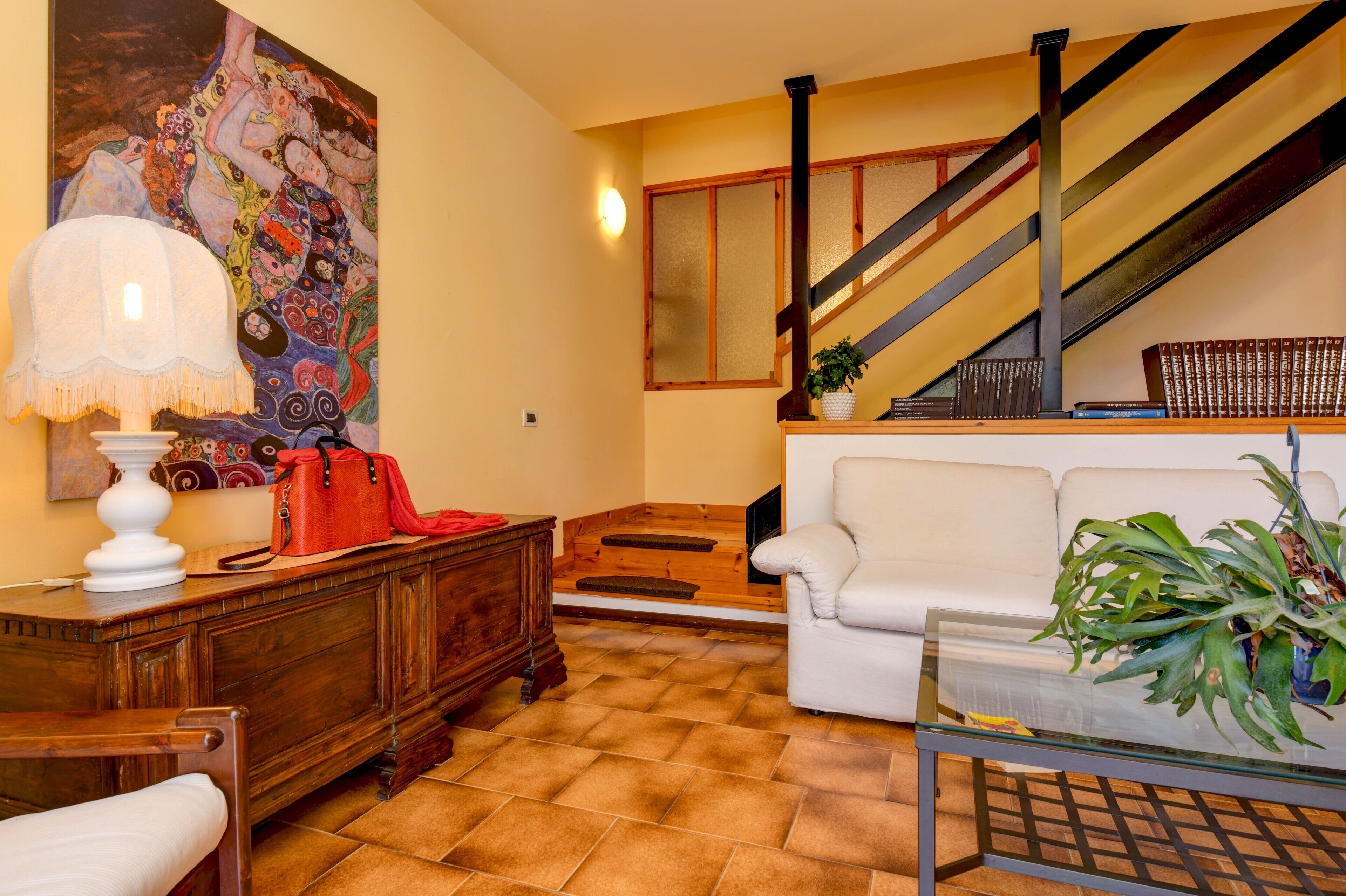 Una sala de estar con una escalera, un sofá blanco, un aparador de madera y un cuadro en la pared.