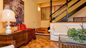 Una sala de estar con una escalera, un sofá blanco, un aparador de madera y un cuadro en la pared.