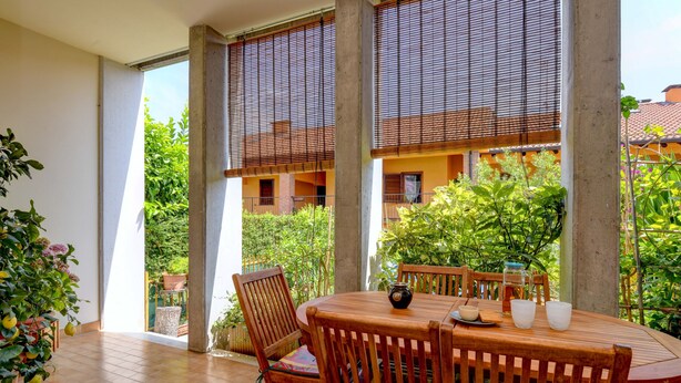 A wooden table and chairs on a balcony with a view of greenery and a building. - Charming Lake Garda Home - Civic 55 (Toscolano Maderno)