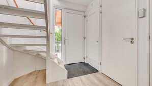Een trap die leidt naar een deur met een cijferslot, een kleed aan de voet ervan en een uitzicht op groen buiten.