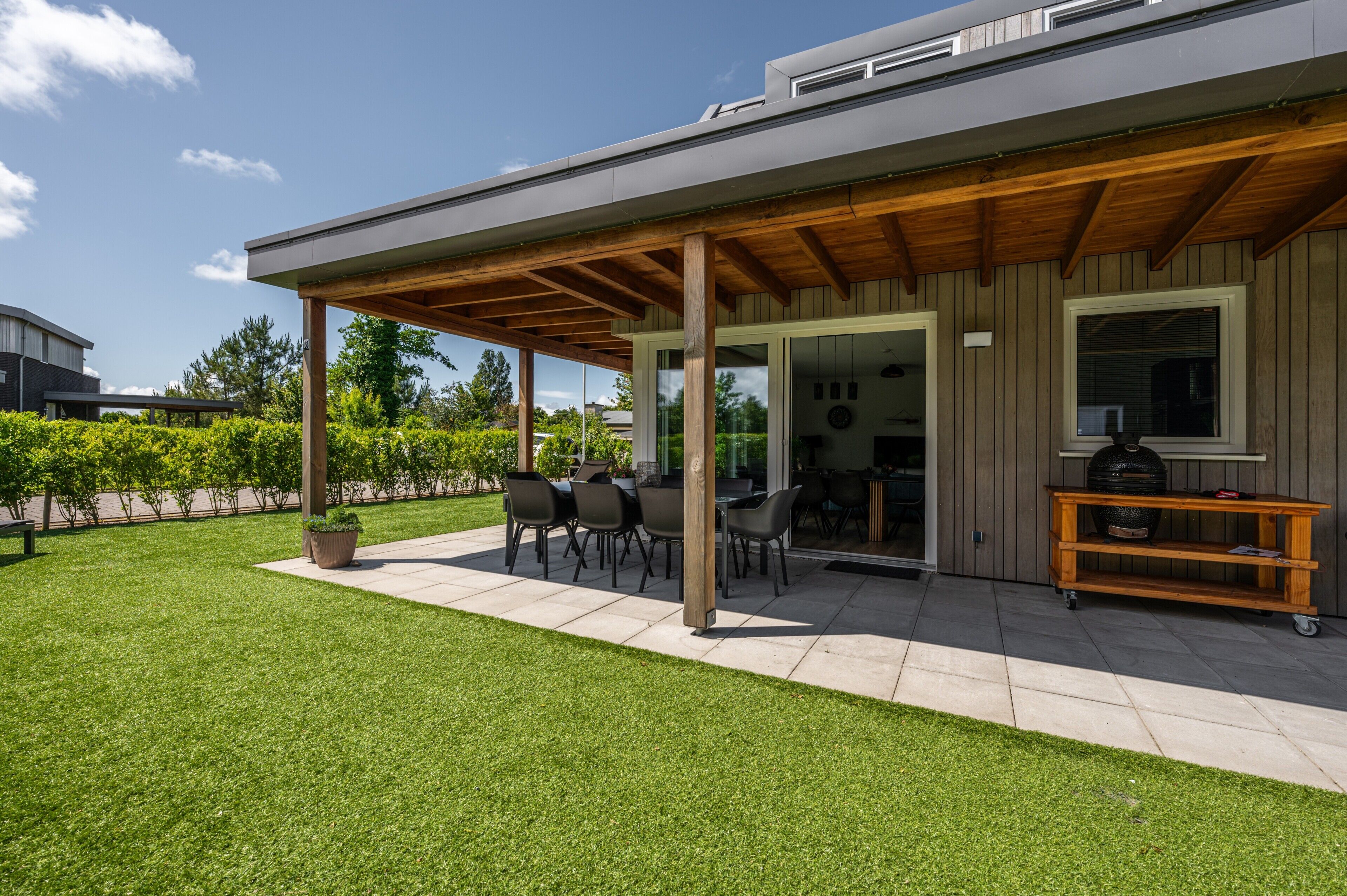 A modern outdoor patio with a covered seating area, a grill, and a well-maintained lawn.