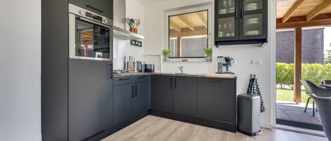 Cocina moderna con gabinetes oscuros, horno empotrado y ventana con persianas.