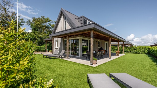 Een modern huis met een overdekt terras, een gazon en tuinmeubilair.