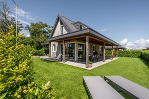 Une maison moderne dotée d’un patio couvert, d’une pelouse et de mobilier d’extérieur.