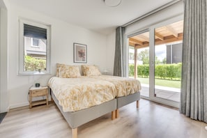 A bedroom with a bed, a bedside table, a window, and a sliding glass door leading to a balcony.