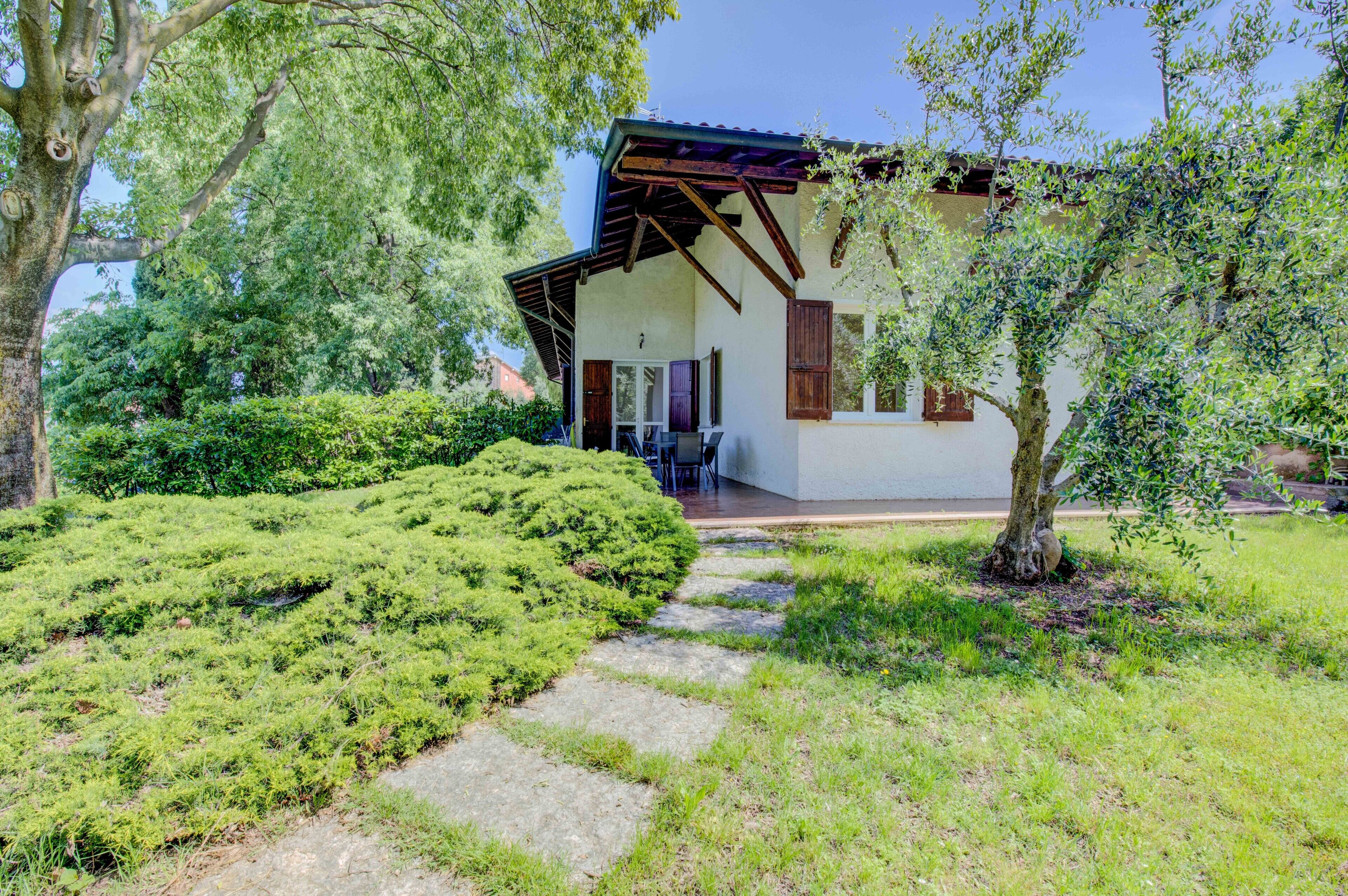 A house with a covered patio, surrounded by lush greenery and a stone pathway.
