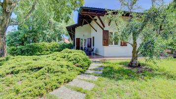 A house with a covered patio, surrounded by lush greenery and a stone pathway.