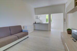 A modern living room with a sofa, a TV, and a remote on a wooden table. - Close to Beach and Trails With Patio - Apartment Rupestre (Manerba del Garda)