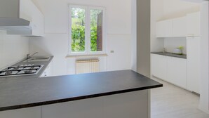 Une cuisine moderne équipée d’une cuisinière à gaz, de meubles blancs et d’une fenêtre donnant sur un espace verdoyant.