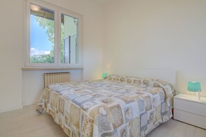 A bedroom with a bed, a window, a radiator, and a nightstand with a lamp. - Close to Beach and Trails With Patio - Apartment Rupestre (Manerba del Garda)