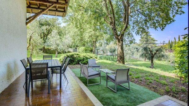 Une terrasse avec une table et des chaises, entourée d’un jardin agrémenté d’arbres et d’arbustes.