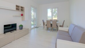 Un salon moderne avec un téléviseur à écran plat, un canapé, une table à manger avec des chaises et une petite plante.