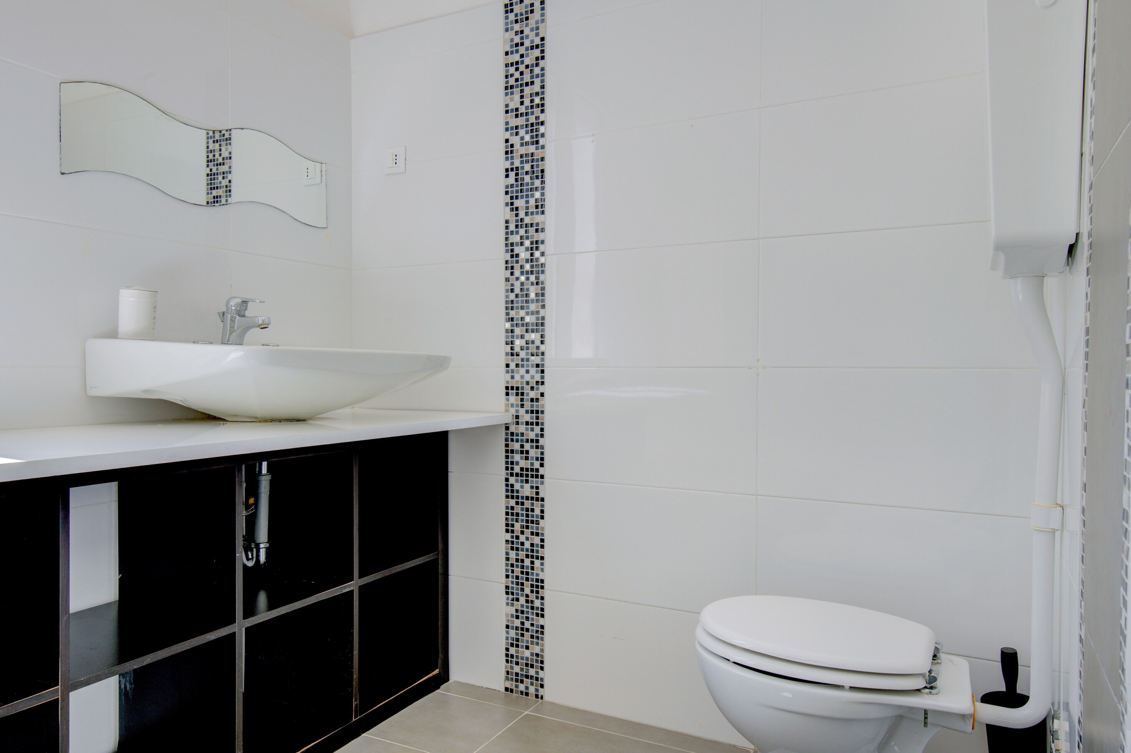 Ein Badezimmer mit einem weißen Waschbecken, schwarzen Schränken, einer weißen Toilette und einer gefliesten Rückwand.