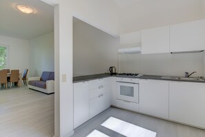 A modern kitchen with white cabinets, a gas stove, and a dining area with a sofa and chairs. - Close to Beach and Trails With Patio - Apartment Rupestre (Manerba del Garda)