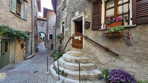 A narrow cobblestone street with stone steps leading to a building entrance, surrounded by traditional architecture. - Beautiful Nature and Historic Center – Liver 203 (Pieve di Tremosine sul Garda Brescia)