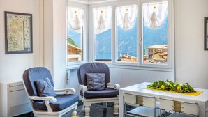 A room with two chairs, a table with a plant, and a window with a view of mountains. - Beautiful Nature and Historic Center – Liver 203 (Pieve di Tremosine sul Garda Brescia)