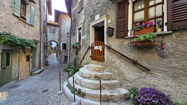 A narrow cobblestone street with stone steps leading to a building entrance, surrounded by traditional architecture. - Mountain Views in the Historic Center - Liver 201 (Pieve di Tremosine sul Garda BS)