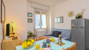 A dining area with a table set for breakfast, a refrigerator, and a sofa in the background. - Mountain Views in the Historic Center - Liver 201 (Pieve di Tremosine sul Garda BS)