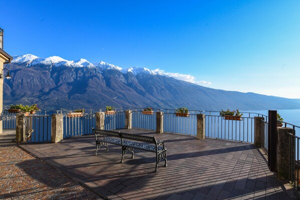 A bench on a paved terrace with a view of snow-capped mountains and a body of water.