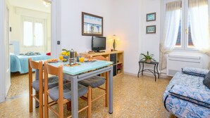 A room with a bed, a desk with a computer, a chair, a table with breakfast items, and a window with curtains. - Mountain Views in the Historic Center - Liver 201 (Pieve di Tremosine sul Garda BS)