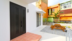 A courtyard with a wooden bench, a tiled patio, and a door with a window. - Annex B Onna (Onna)