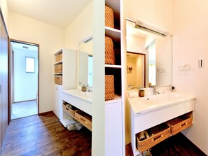 Un baño moderno con muebles blancos, cestas de mimbre y un espejo grande.
