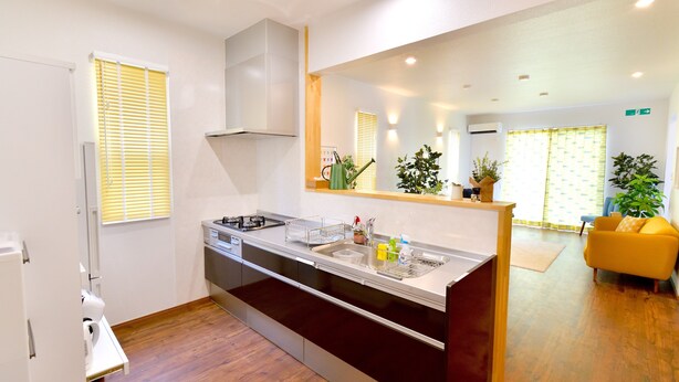 A modern kitchen with a built-in sink, a stove, and a microwave. There is a large mirror above the sink and a yellow sofa in the adjacent living area. - Annex B Onna (Onna)