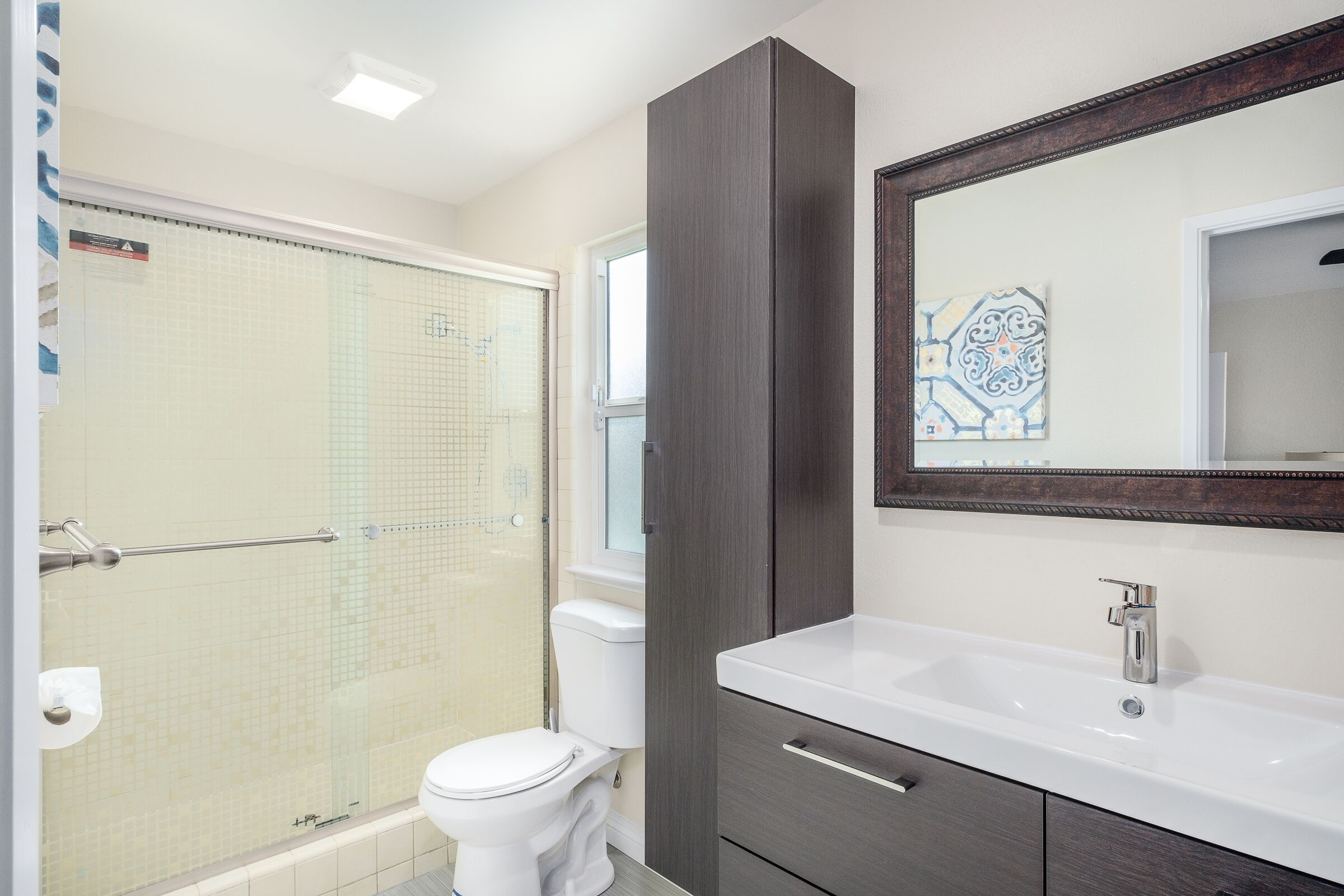 A bathroom with a shower, toilet, vanity, and a large mirror.