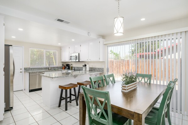 A modern kitchen with white cabinets, a granite countertop, and a dining area with green chairs.