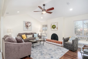 A living room with a sofa, armchair, fireplace, and a ceiling fan.