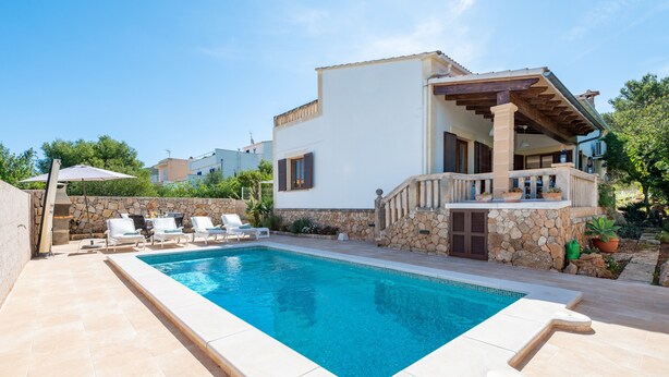 A poolside area with lounge chairs, a stone wall, and a building with a balcony. - Air-Conditioned Holiday Home with Pool, Garden, Terrace & Wi-Fi (Colonia de Sant Pere)