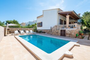 Un espace aménagé au bord de la piscine, avec des chaises longues, un mur en pierre et un bâtiment doté d’un balcon.