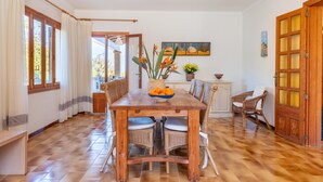 A dining area with a wooden table, wicker chairs, and a bowl of fruit. - Air-Conditioned Holiday Home with Pool, Garden, Terrace & Wi-Fi (Colonia de Sant Pere)