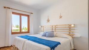 A bedroom with a bed, curtains, a window, a star decoration, and a bedside table. - Air-Conditioned Holiday Home with Pool, Garden, Terrace & Wi-Fi (Colonia de Sant Pere)