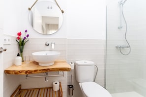 Une salle de bain avec un meuble-lavabo en bois, un lavabo blanc, un miroir, des toilettes et une douche.