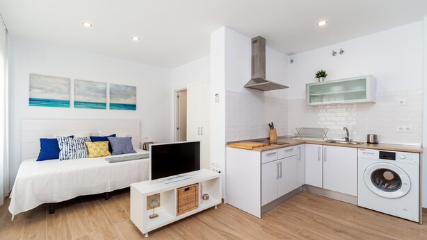 Un espace de vie compact comprenant un lit, une télévision, une kitchenette et un lave-linge.